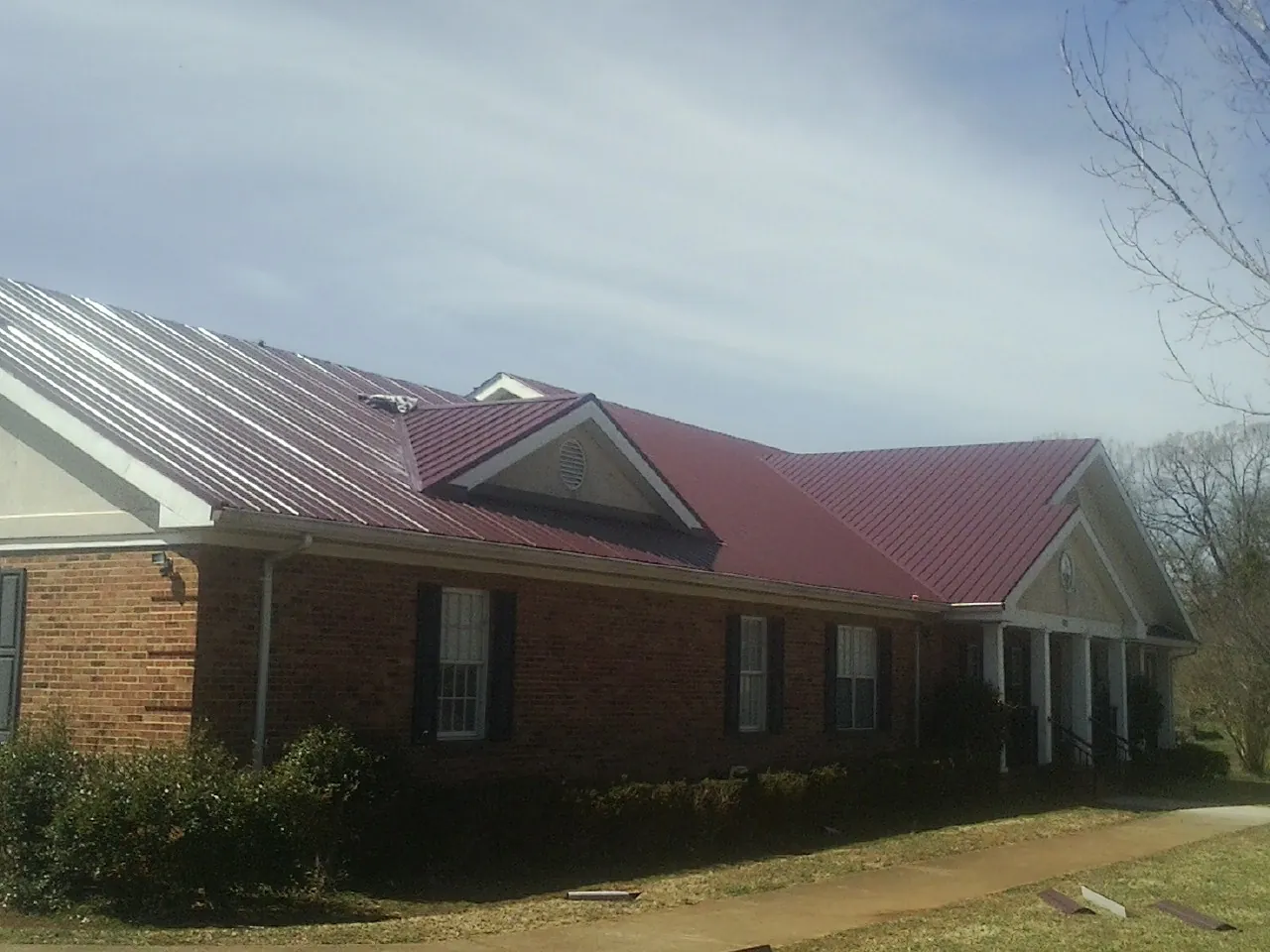 Red metal roof with gabled entries on a long brick building, from a Hail Damage Roof Repair job in Bedford