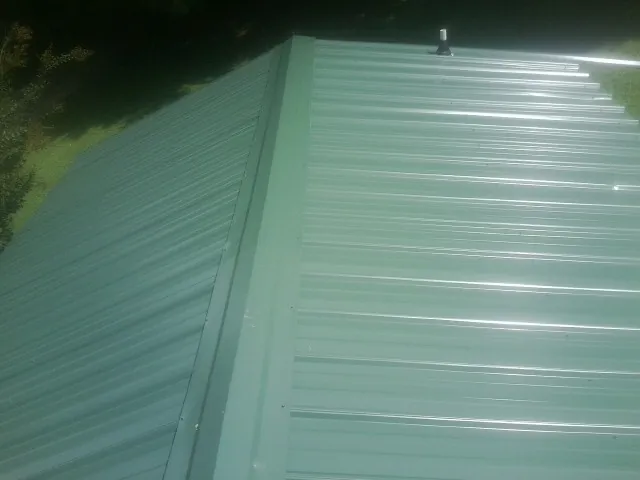 New green metal panels meeting at the ridge of a roof — Flat Roof Repair work by our crew in Bedford